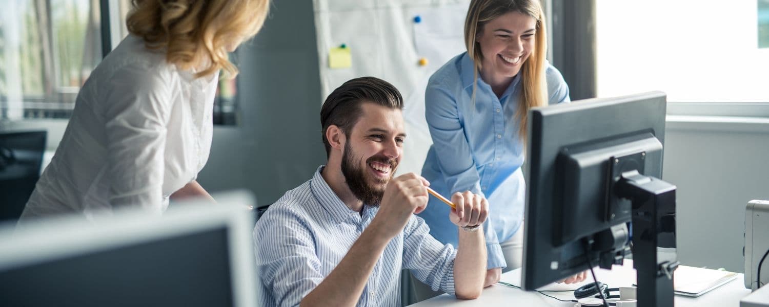 In einem Büro gruppieren sich ein Mann und zwei Frauen um einen Bildschirm.